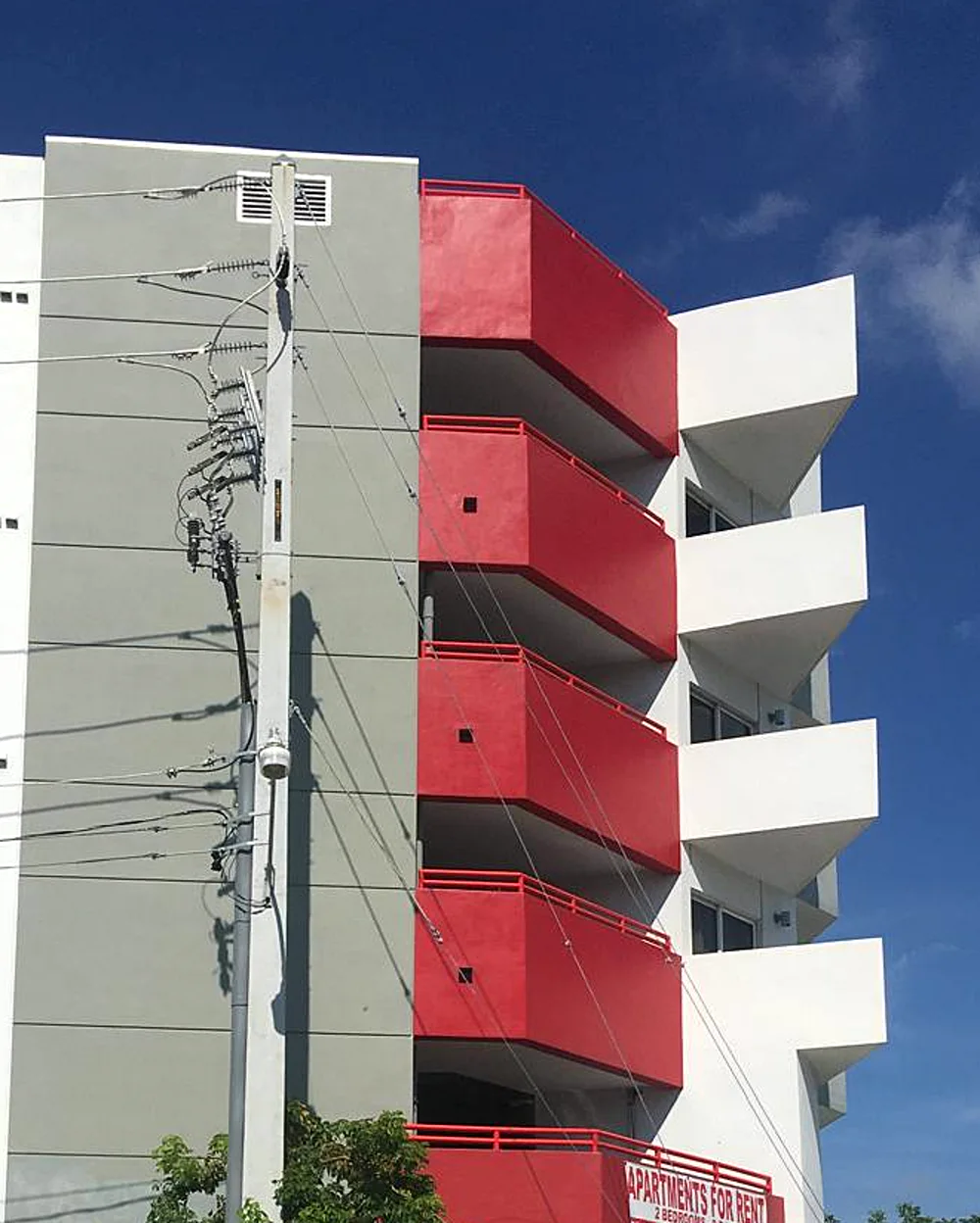 A multi-story apartment building painted white and gray with red balconies
