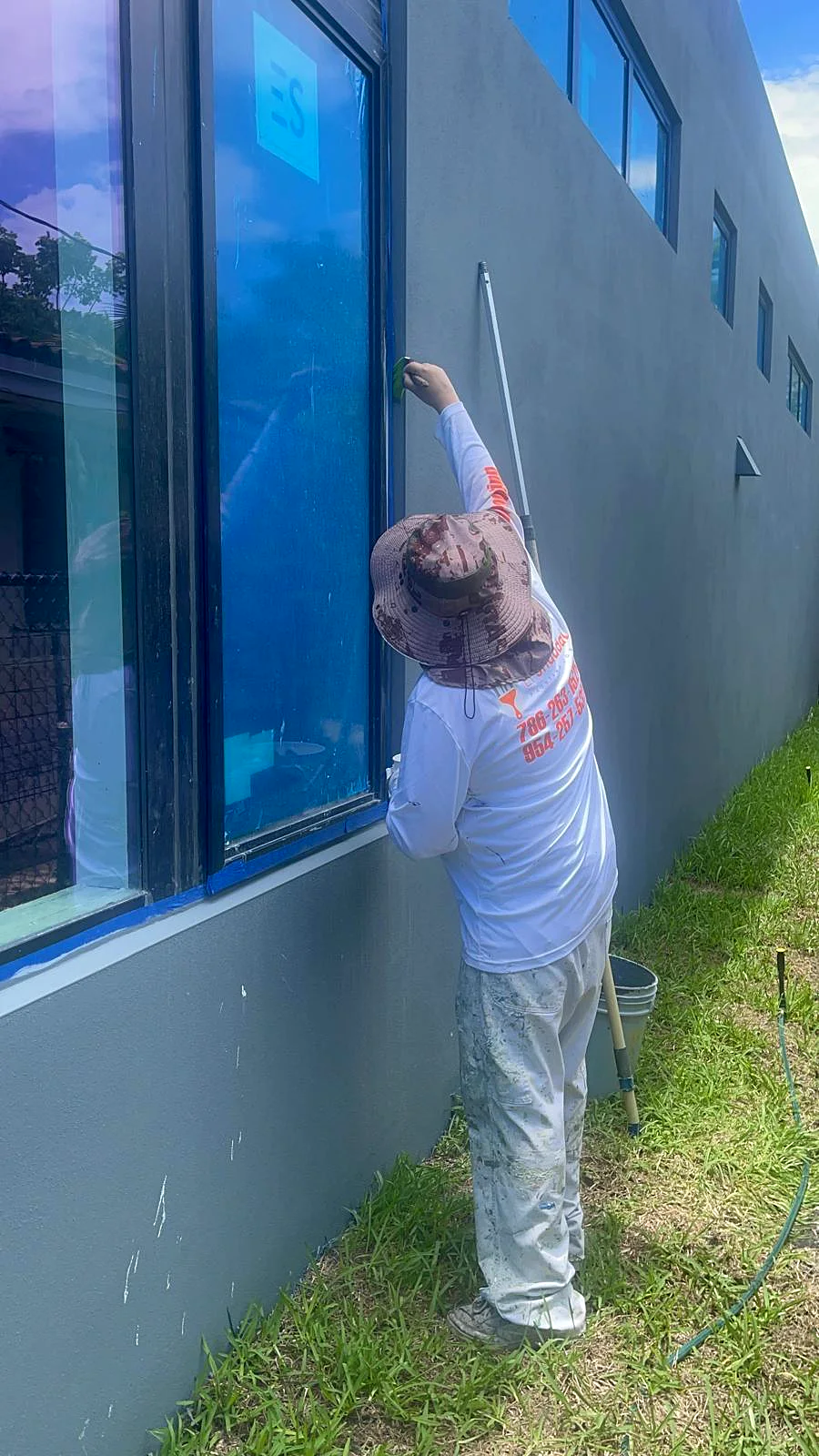 An El Shaddai painter in a company shirt cutting in around a window