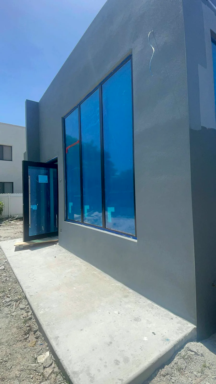 A newly built home with a smooth gray stucco finish and protected windows